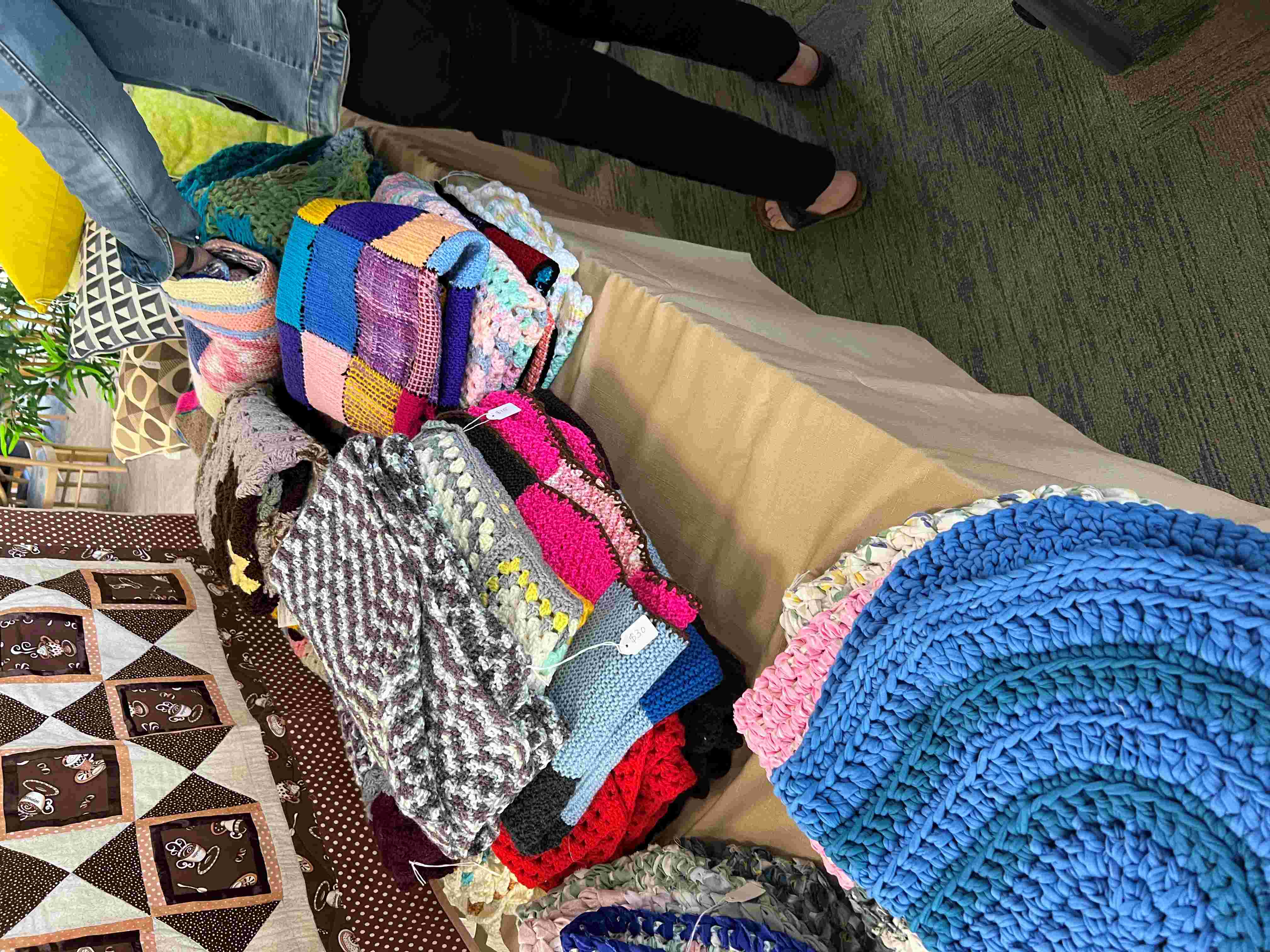 Piles of handcrafted knitted scarves and blankets for sale at a fair.